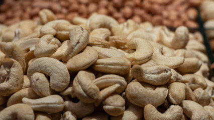 A macro photograph of shelled cashew nuts in a market or store setting. The image captures the creamy color and smooth surface of the cashews, perfect for illustrating healthy eating, vegan diets.