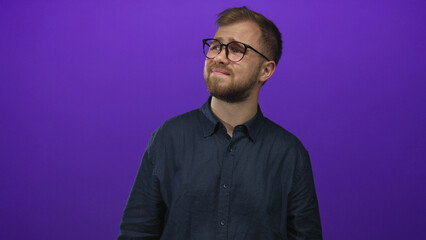 Man wearing glasses and a button shirt with visible face looking up toward a light in purple...