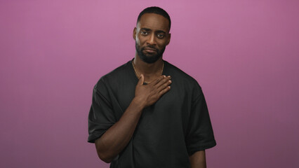 Man with hand over chest in pink studio showing chest touch gesture and pensive expression; regret sincerity.