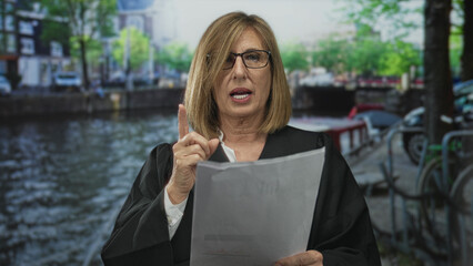 Woman judge in black robe with glasses reading a legal brief by canal street outdoors in city scene...