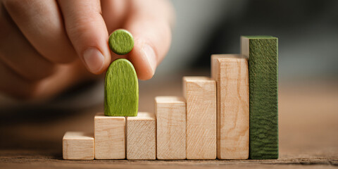 A person carefully positioning a green wooden game piece atop a colorful bar chart to illustrate growth and strategic business planning concepts
