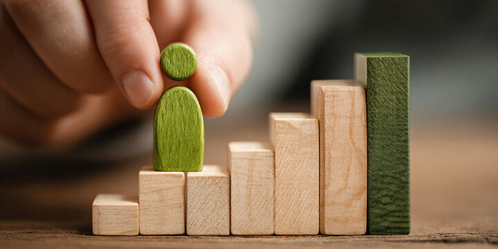 A person carefully positioning a green wooden game piece atop a colorful bar chart to illustrate growth and strategic business planning concepts
