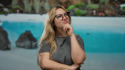 Woman pondering at outdoor resort by a pool in a serene setting with natural beauty, displaying thoughtful expression, sunlight reflecting off the clear water in background