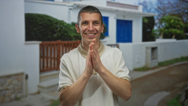 Man smiling outdoors near a suburban house, wearing a casual shirt, surrounded by a peaceful street setting, showcasing joy and positivity in a natural environment.