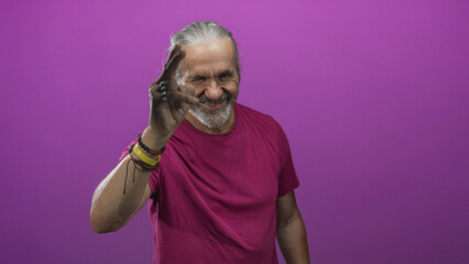 Man raising hand to eye in studio with magenta backdrop making a salute gesture; confidence wisdom charm.
