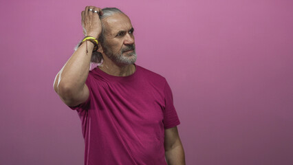 Man with beard and long hair turns head to right in studio with pink background and magenta shirt; quiet contemplation.