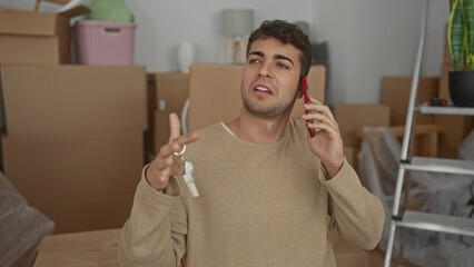 Man lifts phone while talking in home beside hispanic themed boxes as young resident plans moving by unpacking essentials and piles gear like a confident guy.