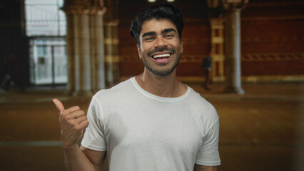 Man in white t shirt pointing thumb to city street under massive stone columns and smiling...