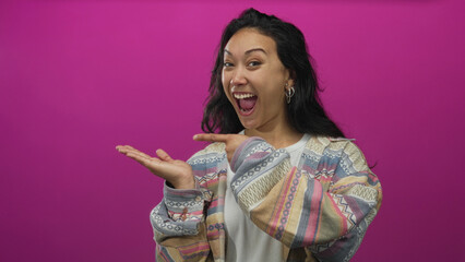 Woman young hispanic presenting open palm and pointing with right hand in studio against magenta...