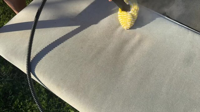 Hand scrubs outdoor furniture with a brush, sunlight casts shadows enhancing texture, spring cleaning vibe with focus on renewal and freshness