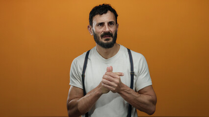 Hispanic man with beard stands against vibrant orange background, wearing white shirt and suspenders, displaying various thoughtful expressions.