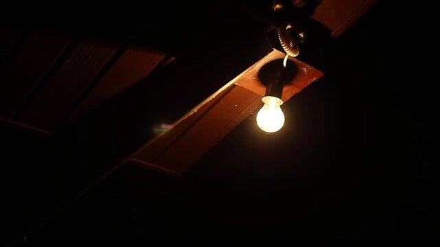 Single glowing bulb hanging under a wooden roof at night. Simple rural life moment, warm and quiet atmosphere of countryside evening.