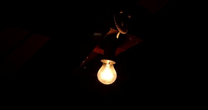 Bright light bulb shining in deep darkness under a wooden structure. Strong contrast of light and shadow, symbol of clarity and focus.