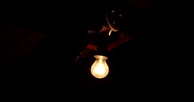 A glowing light bulb under a wooden roof in the dark night. Warm orange light breaking through the blackness, symbol of warmth and hope in darkness.