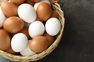 Raw chicken eggs in wicker basket on grey table, above view. Space for text