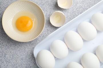 Many whole raw chicken eggs and broken one in bowl on grey table, flat lay
