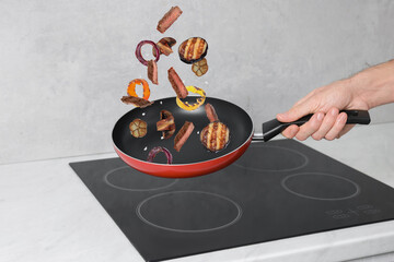 Chef tossing meat and vegetables pieces in frying pan at kitchen, closeup
