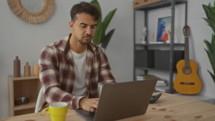 Young man working in a cozy office surrounded by plants and a guitar, exuding a focused and relaxed atmosphere.