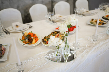 Festive table with various dishes, salads, meat and fish, table setting with flowers in a vase.