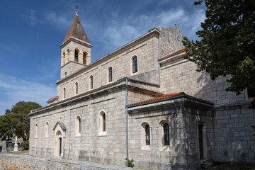 Naklejka premium Stone Church With Bell Tower Surrounded by Green Trees Against a Blue Sky, Grohote, Solta