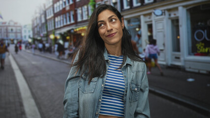 Woman smiling with head tilt and hair blowing, showing face and crop top midriff on a city street; contentment casual urban.