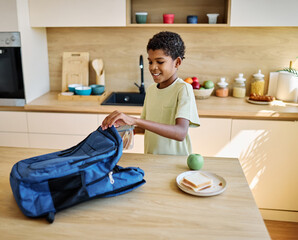 Portret of  a black teen boy with a school backpack having fun alone preparing sanwiches snack for  breakfast and school  in kitchen