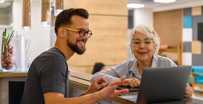 Male doctor showing laptop to smiling senior female patient at reception counter in hospital during visit for eye exam