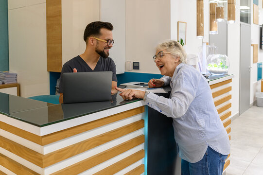 Elderly woman looking at laptop as doctor explains medical details at reception counter in ophthalmology clinic