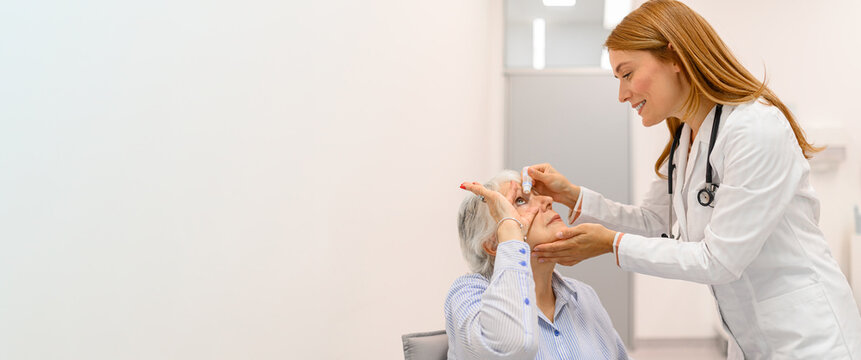 Smiling female ophthalmologist putting eye drops in elderly woman during hospital eye examination