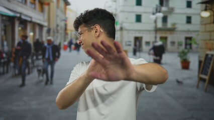 Fototapeta premium Man pushes forward his hands in a stop gesture and grimaces adjusting his glasses on a crowded urban street; rejection.