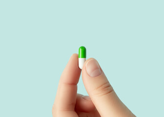 Hand holding a green and white medicine capsule close up