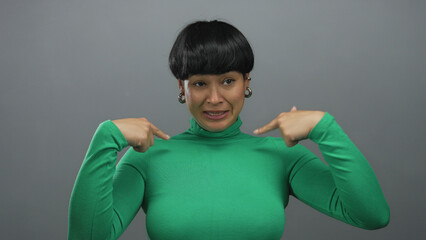 Woman in green sweater gesturing against isolated grey background expresses emotions with hands and...