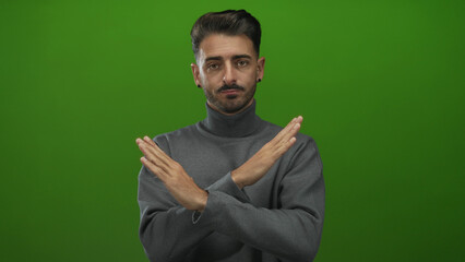 Young hispanic man in grey turtleneck with crossed arms and black earrings in studio; denial...