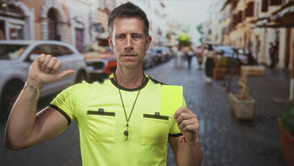 Man referee holding yellow card and whistle on street, thumb pointing to card; authority discipline...