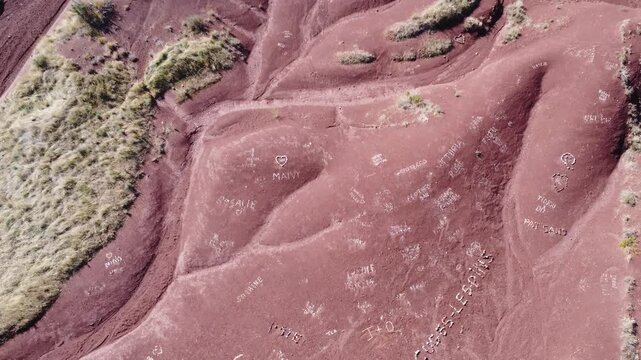 Descending aerial view of the red ruffes of Salagou Lake, where tourists have arranged white stones into messages on the iron-rich soil. Unique blend of nature and human presence. Check my portfolio f
