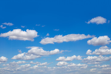 Fluffy white cumulus clouds float across a bright blue sky, creating a picturesque celestial landscape