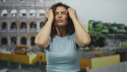 Woman presses temples with both hands and closes eyes outside the roman colosseum building in...