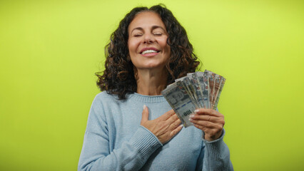 Middle-aged woman in peru holds peruvian soles with one hand on her chest, smiling against a bright...