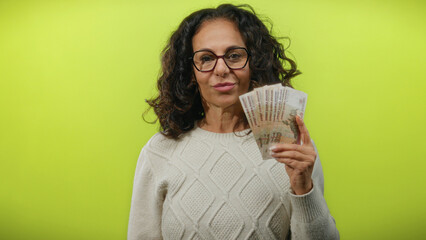 Middle-aged woman holding russian rubles in front of a plain yellow wall, showcasing currency and...