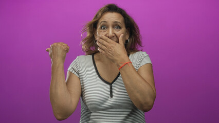 Middle age hispanic woman covers mouth with hand and raises eyebrows and makes direct eye contact...