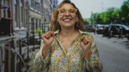 Woman wearing floral shirt and glasses clenches fists on city street amid parked cars and building...