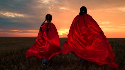 Kids runs in superhero costume in nature park. Happy children run across meadow in red superhero capes. Little girls in red capes play superheroes in field at sunset. Game concept for kids. Freedom