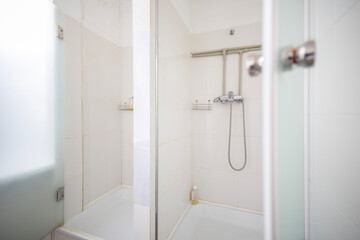 A clean and modern public shower stall with white tiles and a glass door. The functional design highlights practical amenities for hygiene in a shared space like a gym or hostel.