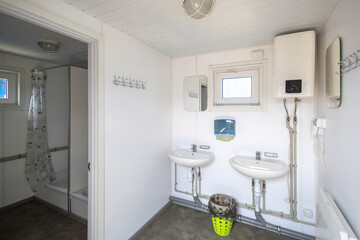 A clean, functional shared washroom in a modular cabin with twin sinks, a water heater, and an adjoining shower stall. This practical setup provides essential hygiene amenities for temporary housing.