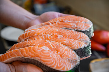 Freshly cut salmon steaks held in a chef’s hands in a kitchen, ready for cooking or seasoning.