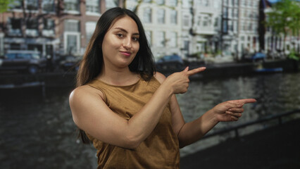 Woman points finger to canal on an amsterdam street with a smirk and shrugged shoulders; playful...