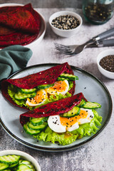 Beetroot chia pancakes with poached egg, cucumber and lettuce on a plate vertical view
