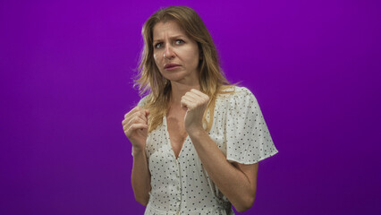 Woman with clenched fists and hands near face in a studio against a purple wall; anxiety worry unease.