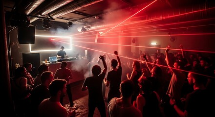 An energetic crowd of people dancing in a dark nightclub with a DJ performing under red laser lights.