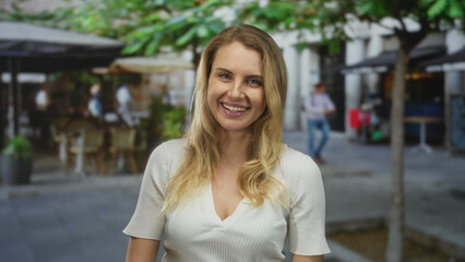 Fototapeta premium Woman smiling on urban street with blonde hair wearing white shirt outdoors in city setting showing casual happiness in lively environment under sunny sky with blurred background.